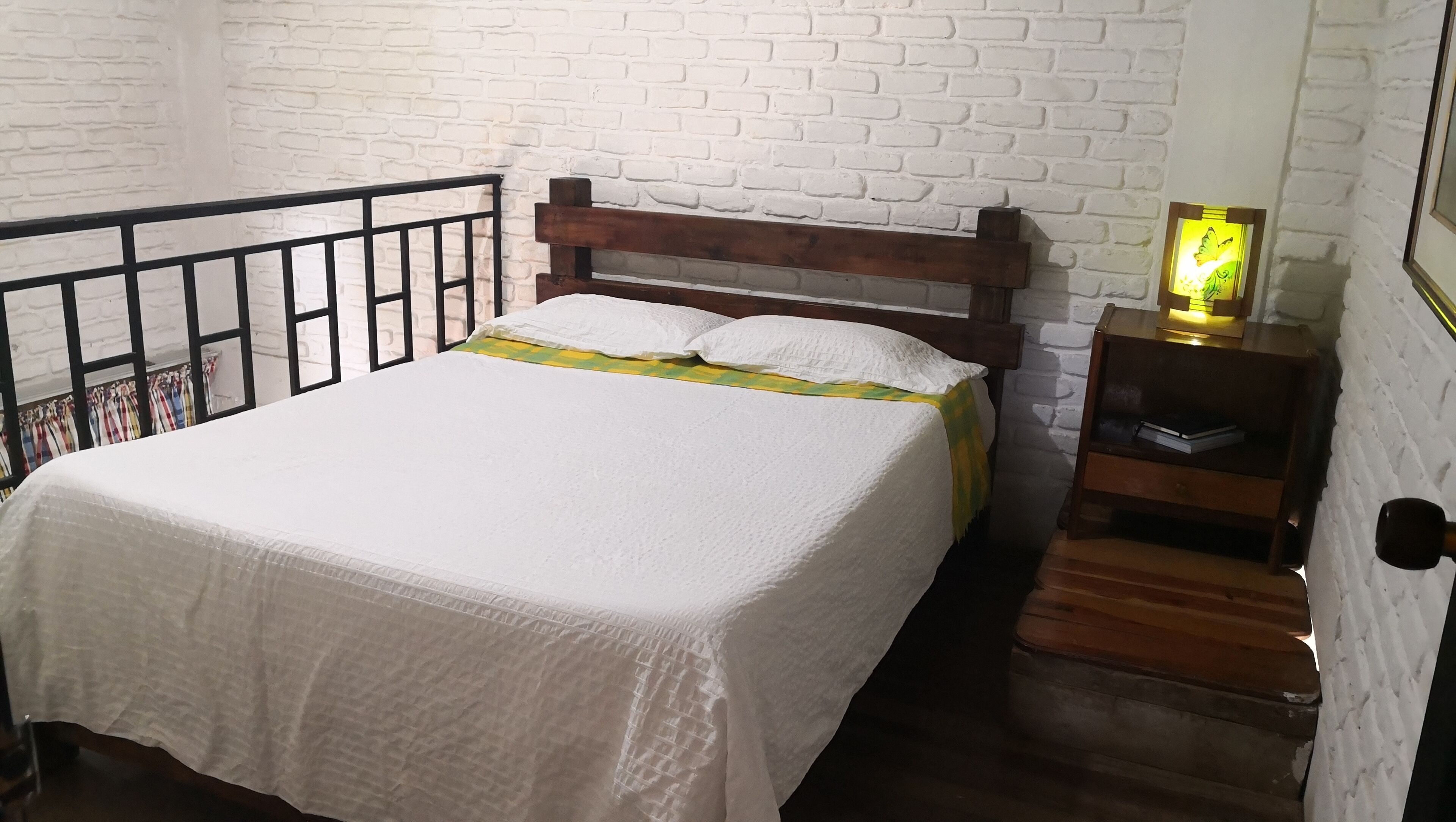 A bed with a wooden headboard, white bedding, and a nightstand with a lamp.