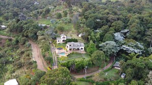 A large house surrounded by dense forest, with a visible swimming pool and a paved driveway.