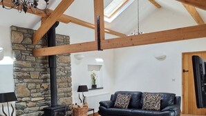 A spacious loft with exposed wooden beams, a stone fireplace, and a cozy seating area with a black leather sofa and ottoman.