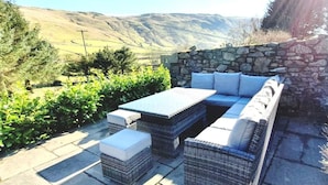 An outdoor patio with a stone wall, wicker furniture, and a view of hills.