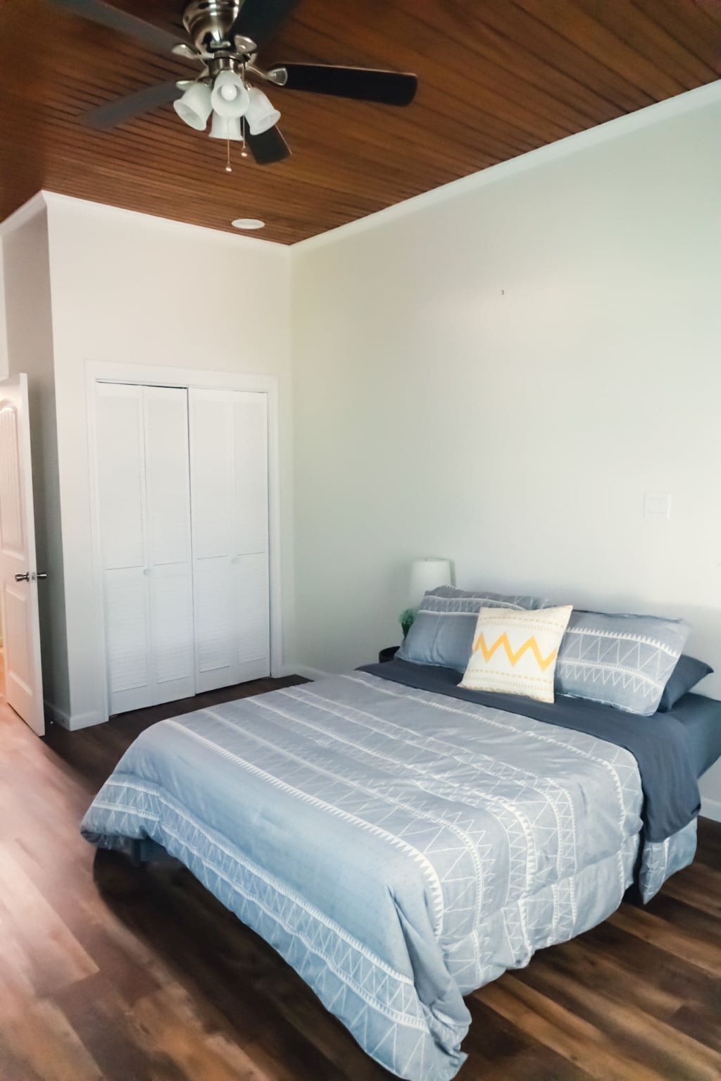 A bedroom with a bed, a ceiling fan, a wardrobe, and a nightstand.