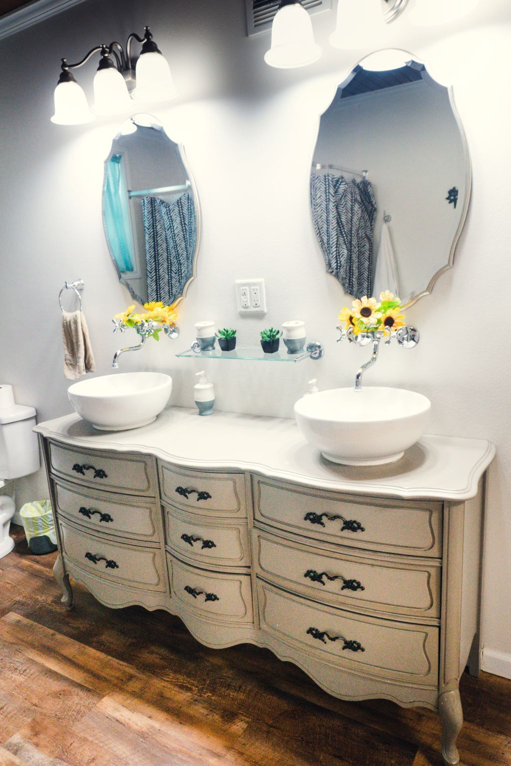 Un bagno con due lavandini, un mobile contenitore con cassetti, uno specchio e un lampadario.