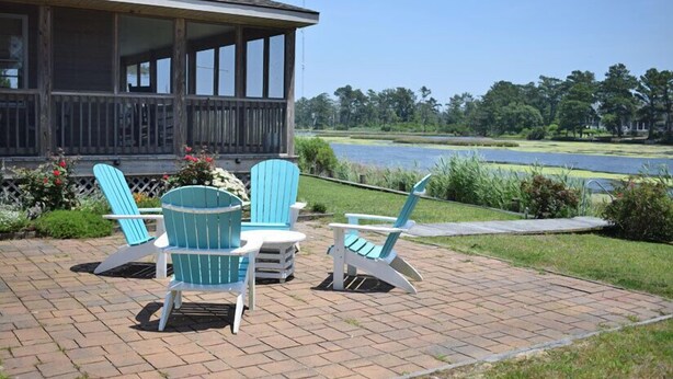 Eine überdachte Terrasse mit Adirondack-Stühlen und einem Tisch, mit Blick auf einen See und einen Golfplatz.