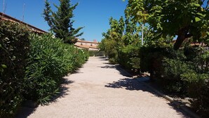 A paved pathway flanked by dense greenery and a building in the background. - Villa in secure residence with swimming pool 200m from the beach (Saint-Cyprien)