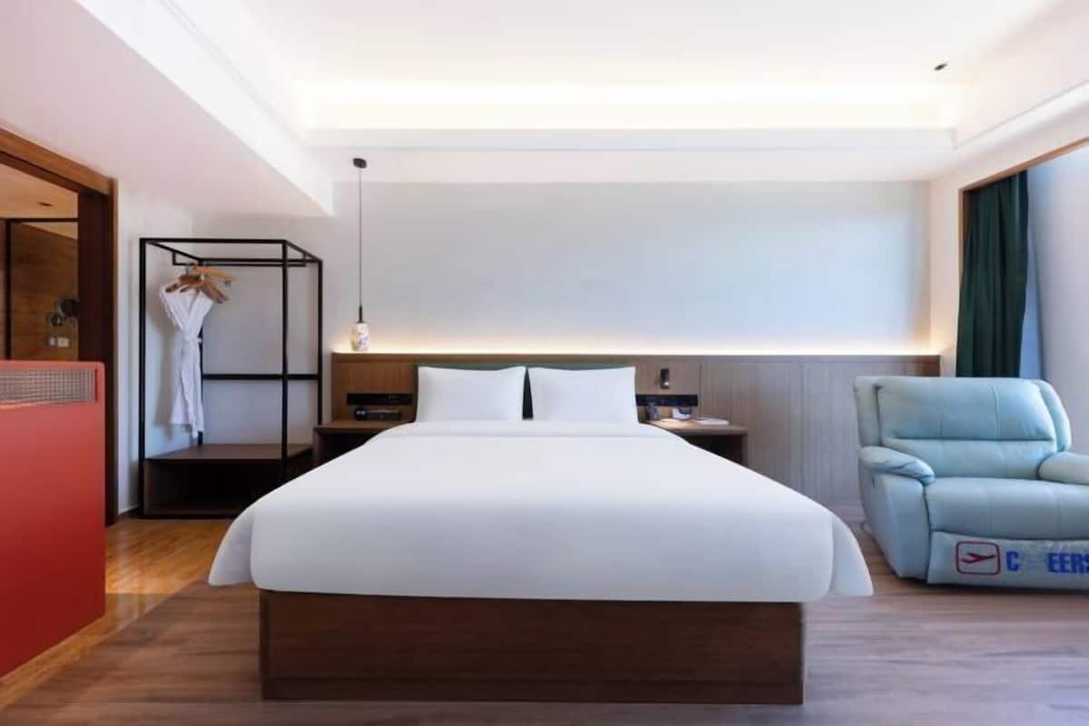 Habitación de hotel con cama grande, armario, zona de estar y escritorio con lámpara.