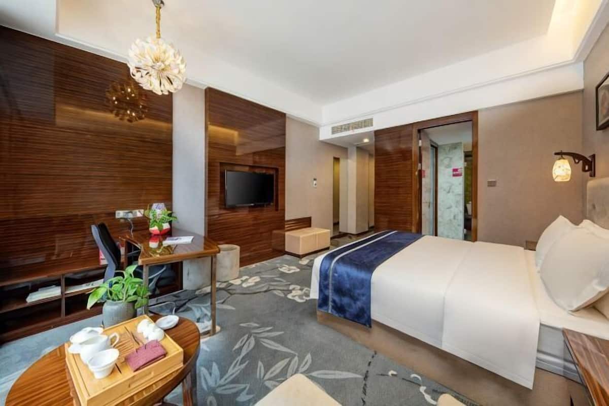 Una habitación de hotel moderna con cama, escritorio, televisor y zona de comedor con mesa y sillas.