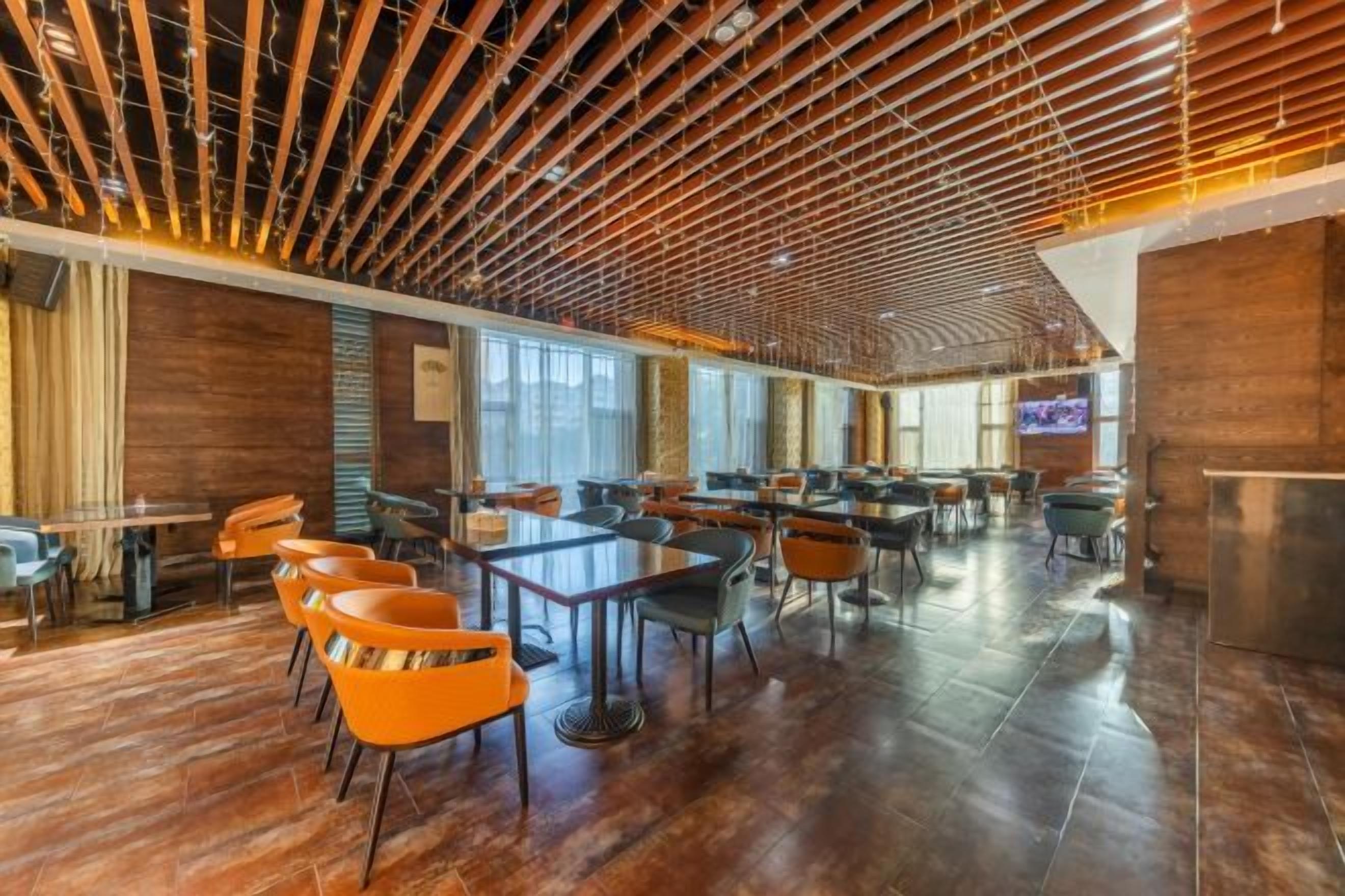 A spacious indoor area with multiple tables and chairs, wooden ceiling beams, and large windows.