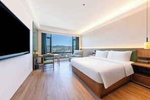 A modern hotel room with a large bed, a desk, and a view of the city. - Dehua Meiyuan International Hotel (Hongqifang Ceramic Tourism Store) (Dehua)