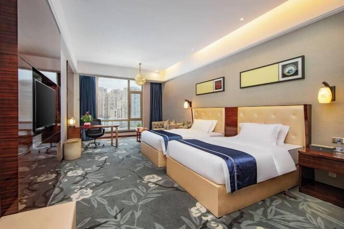 Habitación de hotel con una cama grande, un escritorio, una silla, un televisor y vistas a la ciudad.