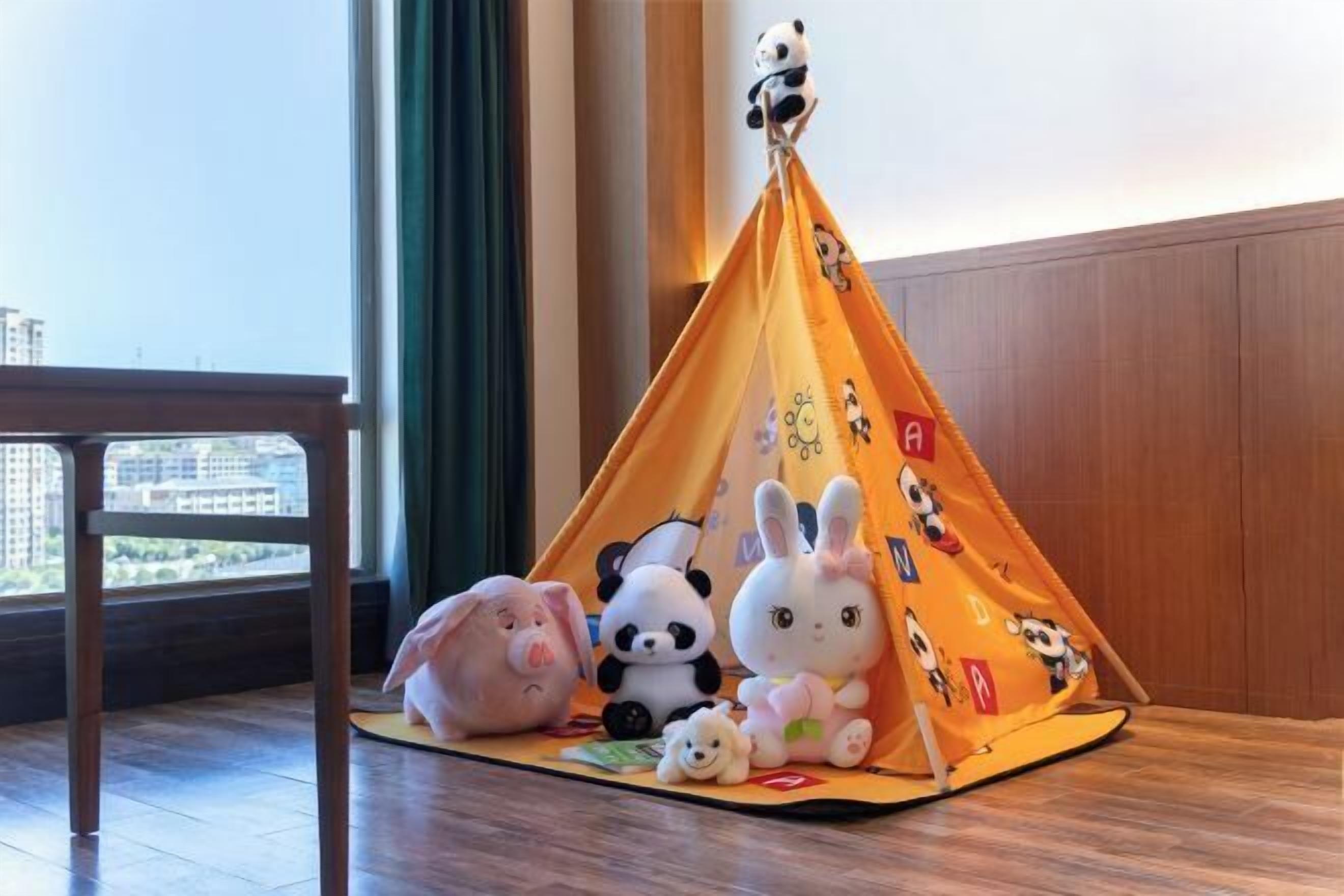 A tent with plush toys inside, placed on a wooden floor near a window with a view of buildings.