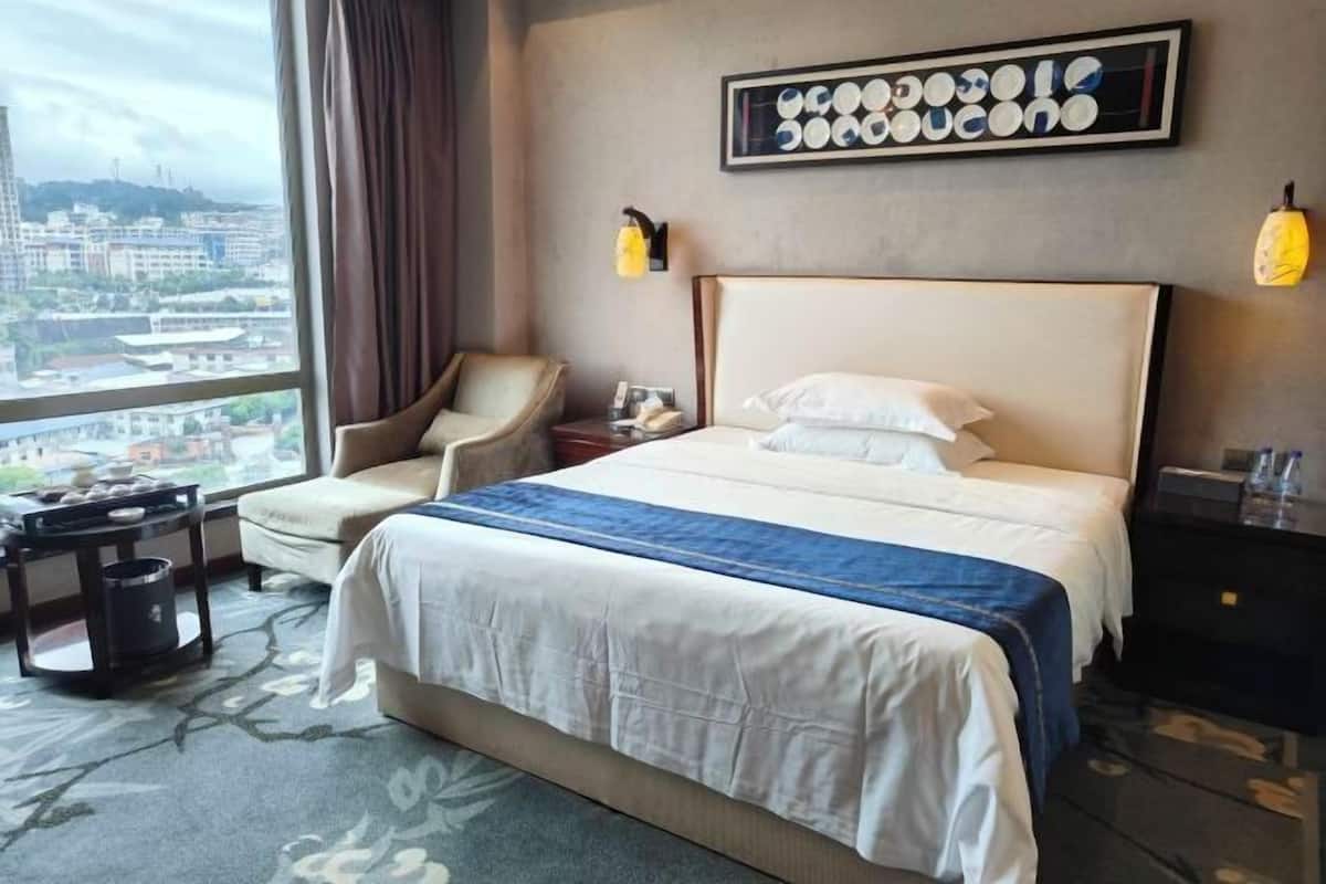 Una habitación de hotel con una cama grande, una silla, un escritorio y vistas a la ciudad.