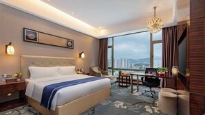 Habitación de hotel con cama, escritorio, silla y ventana grande con vista a la ciudad.