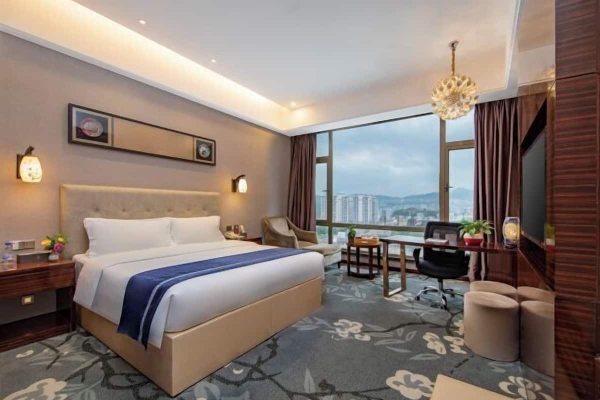 Habitación de hotel con cama, escritorio, silla y ventana grande con vista a la ciudad.