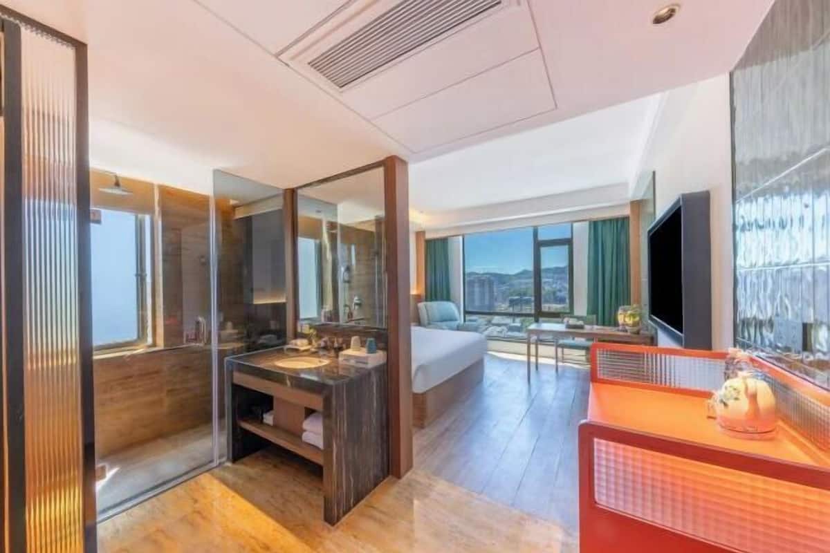 Una habitación de hotel moderna con una cama grande, un baño con tocador, televisión y vistas a la ciudad.