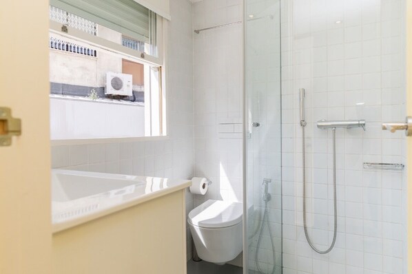 Une salle de bain moderne avec une douche à parois de verre, des toilettes et une fenêtre au-dessus du lavabo.