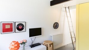 A modern room with a white wall, a mounted television, a red framed award, a vinyl record, a decorative orange vase, and a wooden ladder. - VIVA Casinha da Foz - Close to the beach (Porto)