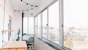 Una camera moderna con un tavolo in legno, una sedia, un cactus e vista sulla città attraverso ampie finestre.