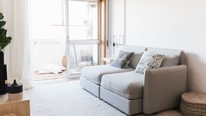 Un soggiorno moderno con un divano grigio, un poggiapiedi rotondo e una porta scorrevole in vetro che dà su uno spazio all'aperto.