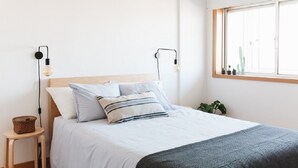 Un letto rifatto con cura, una testiera in legno, due lampade sui comodini, uno sgabello di legno e una finestra con vista su un cactus.