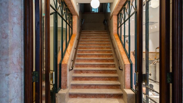 A grand staircase with marble steps and glass railings, leading to a second floor.