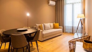 A modern living room with a round dining table, a sofa with cushions, a standing lamp, and an air conditioning unit.