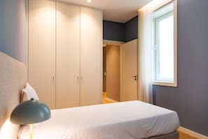 Ein Schlafzimmer mit einem Bett, einer Nachttischlampe, einem Kleiderschrank und einem Fenster.