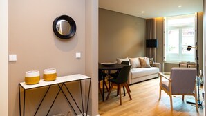 Ein modernes Wohnzimmer mit einer Couch, einem Esstisch und Stühlen. Ein Fernseher ist an der Wand befestigt und es gibt ein Fenster mit Vorhängen.