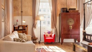 Una sala acogedora con un sofá, un sillón rojo, un aparador de madera y una lámpara de pie.