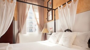 Habitación de hotel con cama con dosel, una lámpara y vistas a edificios a través del ventanal.