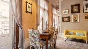 Un área de comedor con una mesa de madera y sillas florales, un sofá amarillo y obras de arte en las paredes.