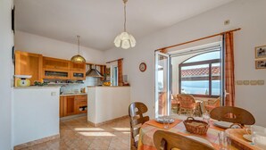 A kitchen with wooden cabinets, a sink, and a dining area with a table set for two. - Beach front home in Jesenice (Jesenice)