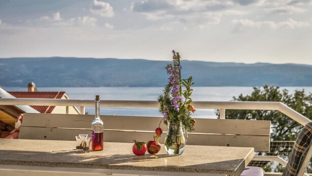 A table with a bottle, glasses, and a vase with flowers and fruit. - Beach front home in Jesenice (Jesenice)