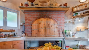 A kitchen with a brick oven, wooden cabinets, and a fruit bowl on the counter. - Beach front home in Jesenice (Jesenice)