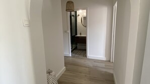 Un couloir doté d’un plancher en bois, de murs blancs et d’une porte en arc donnant sur une salle de bain équipée d’un miroir et d’un lavabo.