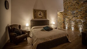 Un dormitorio con pared de piedra, una cama con cabecera, una silla y dos lámparas de noche.