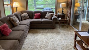 Ein Wohnzimmer mit Ecksofa, einer Uhr, einer Lampe und Seeblick durch ein Fenster.