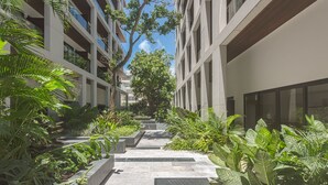 A modern building with a central courtyard featuring a stone pathway, surrounded by lush greenery and large windows. - Awesome Location for 5th AVE & BEACH access without  noise! INCREDIBLE ROOFTOP (Playa Del Carmen, Solidaridad)