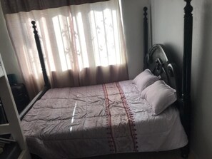 A bed with a headboard, a window with curtains, and a wooden floor. - Welcome to a beautiful place ~ KareBer Abode (Gulu)