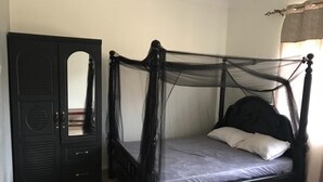 Un lit à baldaquin, une armoire noire avec des portes miroir et un sol carrelé de couleur claire.