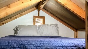 Un dormitorio acogedor y pequeño en el ático, con techo de madera y una cama individual con colcha azul.