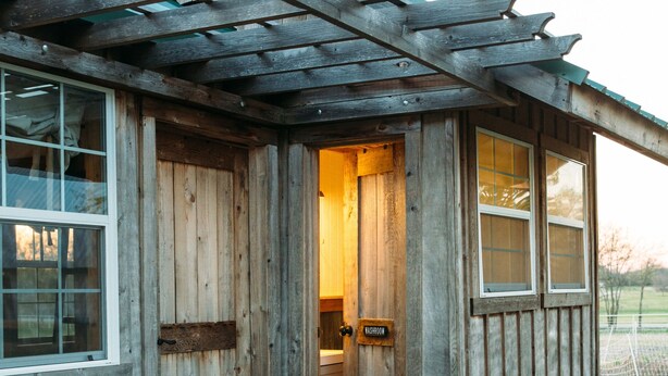 Una cabaña de madera con porche de madera, una puerta y una ventana.