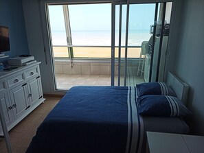 A bedroom with a large bed, a TV on a cabinet, and a view of the beach through a sliding door.