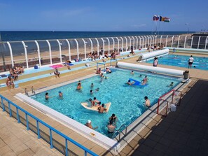A pool area with multiple swimming pools, a beach, and a clear sky.