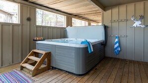 Un bain à remous dans un espace extérieur abrité, doté d’un plancher en bois, d’un escalier en bois et d’une serviette accrochée au mur.