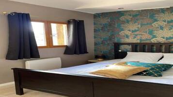 Un dormitorio con una cama, cortinas, un ventanal y una pared con estampado floral.