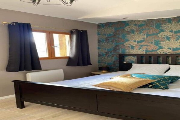 Un dormitorio con una cama, cortinas, un ventanal y una pared con estampado floral.