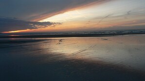 Una playa con arena mojada y un atardecer al fondo.