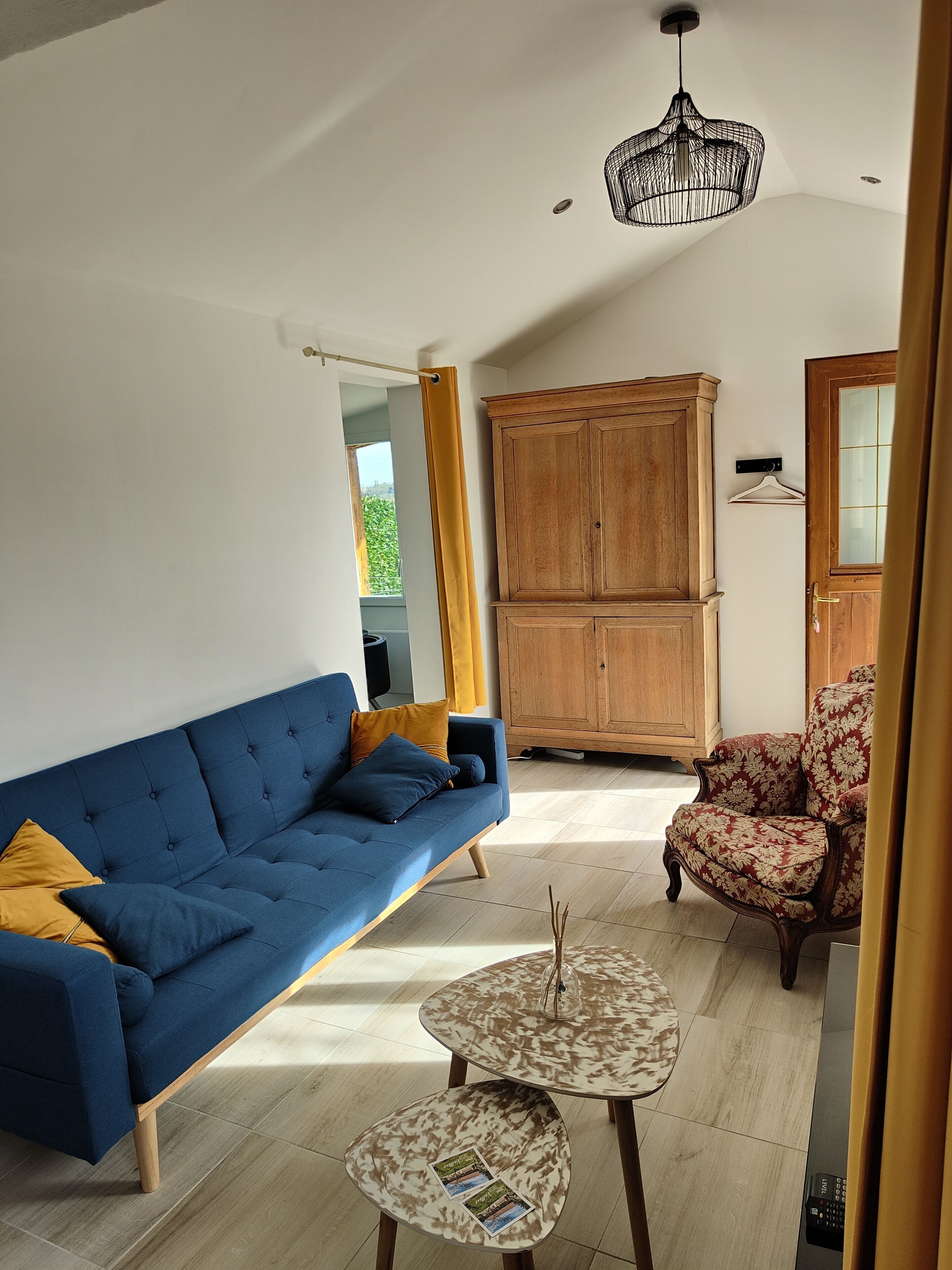 Ein Wohnzimmer mit einem blauen Sofa, einem Couchtisch mit Muster, einem Holzschrank und einem floralen Sessel.
