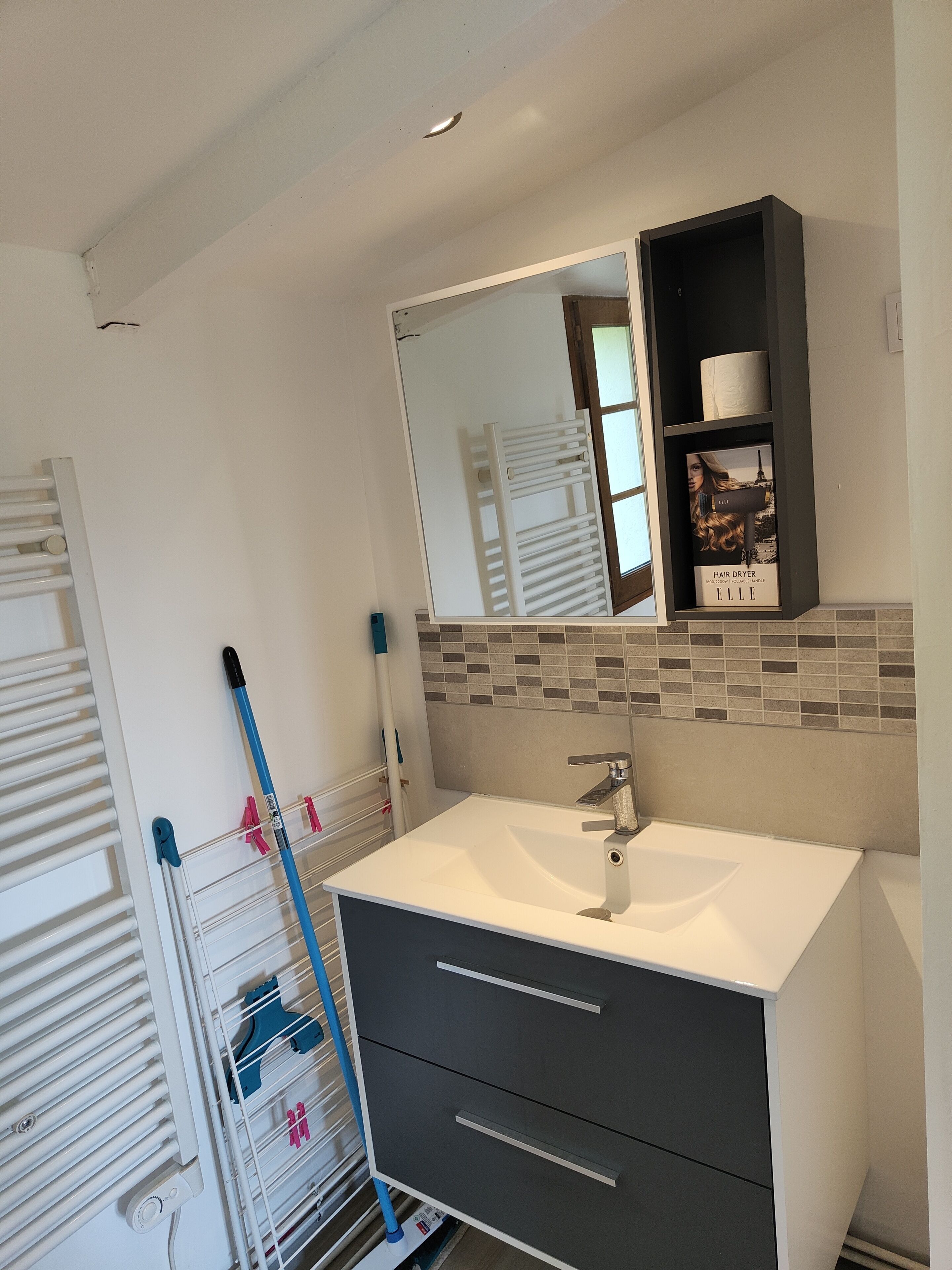 A bathroom with a white sink, a mirror, a towel rack, and a hair dryer on the wall.