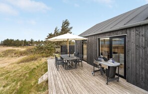 Une terrasse en bois avec une table et des chaises, un barbecue et un grand parasol.